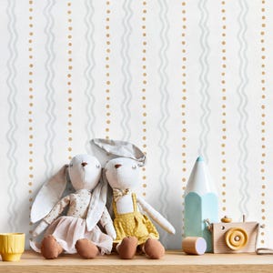 May include: Wallpaper featuring a repeating pattern of vertical light gray wavy lines alternating with vertical rows of small mustard yellow dots on a white background, displayed behind two plush rabbit dolls and wooden toys.