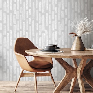 May include: A dining room scene featuring a round wooden table with a brown leather chair. The table is set with gray plates and bowls. The background is a gray wall with a white pattern. A bronze vase holds dried flowers.