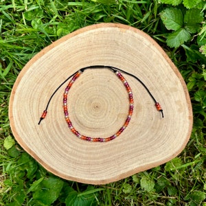 May include: A multi-colored beaded bracelet with a black cord. The beads are red, orange, and silver.