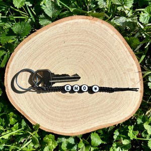 May include: Black and white beaded keychain with the word "EMO" and a star charm. The keychain is attached to a silver key.