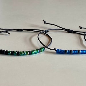 May include: Four adjustable bracelets with black string and colorful beads. The bracelets feature red, green, blue, and black beads.