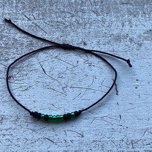 Peut inclure: Un bracelet en cordon noir avec une rangée de petites perles vertes irisées.