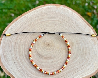 May include: A white and orange beaded bracelet with gold accents on a black cord.