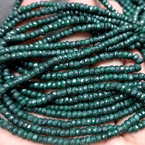 May include: A strand of dark green faceted beads. The beads are small and round, and they are strung together on a clear thread.