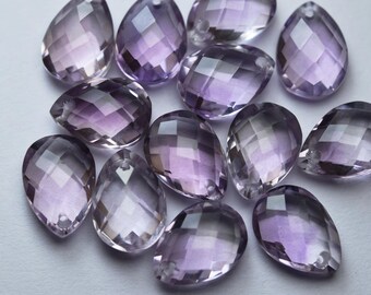 May include: A collection of eleven translucent, light purple, teardrop-shaped beads with a faceted surface. Each bead features a small, circular hole at the top point, designed for stringing. The beads exhibit varying shades of lavender and violet.