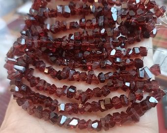 May include: Strands of faceted, dark red garnet gemstone beads. The beads are irregularly shaped and strung together, showcasing a rich, deep color. These beads are ideal for jewelry making.