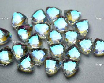 Puede incluir: Un grupo de piedras preciosas iridiscentes, transparentes, facetadas, en forma de corazón. Las piedras preciosas están esparcidas sobre una superficie gris.