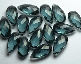 May include: A group of 15 teal blue faceted teardrop shaped gemstone beads. The beads are all approximately the same size and shape.