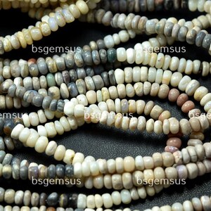 May include: A strand of white, gray, and brown opal beads. The beads are small and round, and they are strung on a clear thread. The beads are arranged in a random pattern, and they are all different sizes. The beads are a natural color, and they have a smooth, polished finish.