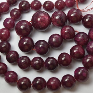 May include: A strand of deep red gemstone beads. The beads are round and smooth, with a slight sheen. The beads are strung on a thin red thread.