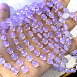 Könnte beinhalten: Stränge hellvioletter, ovaler Perlen mit goldfarbenen Abstandshaltern. Die Perlen sind aufgefädelt, für eine Halskette oder ein Armband. Die Perlen werden in einer Hand gehalten.