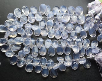 May include: A strand of light purple gemstone beads, each bead is a teardrop shape with a faceted finish. The beads are strung on a white thread and are approximately 18 mm in length. The beads are displayed on a black surface with a purple tassel on the right side of the image. The text "https://www.etsy.com/in-en/shop/BSGEMSUS" is repeated three times on the image.
