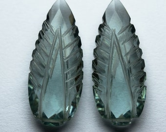 May include: Two carved teal green gemstone pendants in the shape of a leaf. The leaves have a detailed carved design.