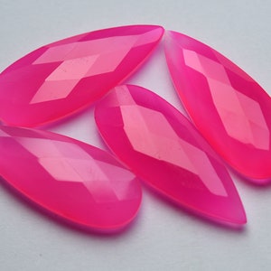 Puede incluir: Cuatro gemas facetadas en forma de lágrima, de color rosa intenso, dispuestas sobre una superficie blanca. Las gemas tienen un aspecto pulido y translúcido con múltiples facetas que captan la luz, creando un efecto brillante. Ideales para la fabricación de joyas.