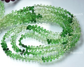May include: Strands of green gemstone beads in varying shades, from light to dark, arranged in a flowing pattern. The beads are teardrop-shaped and appear to be strung together. The overall effect is one of natural beauty and elegance.