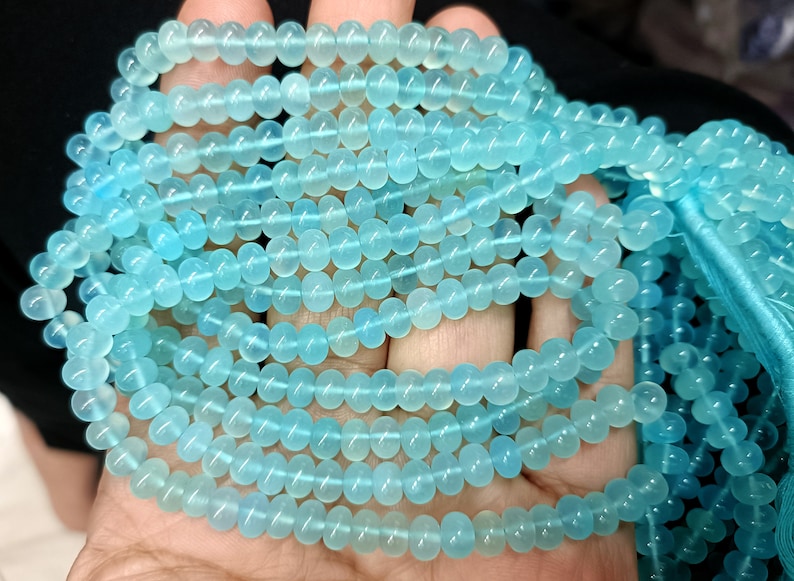 May include: A strand of light blue gemstone beads. The beads are round and smooth, and they have a translucent appearance.