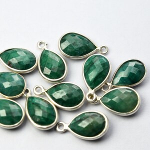 May include: A group of 11 green gemstone pendants with silver settings. The gemstones are faceted and have a teardrop shape. The pendants are perfect for jewelry making.