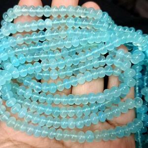 May include: A strand of light blue gemstone beads. The beads are round and smooth, and they have a translucent appearance.