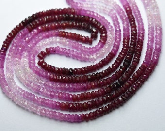 May include: Several strands of faceted gemstone beads in shades of pink and red are arranged in a spiral pattern. The beads transition from light pink to deep red, creating a gradient effect. The beads are small and uniform in size.