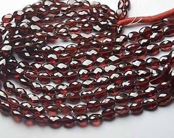 May include: A strand of dark red gemstone beads, each bead is faceted and oval shaped. The beads are strung on a thin cord.