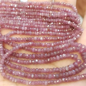 Può includere: Un filo di perle di rubino rosa, sfaccettate e infilate su un filo. Le perle sono piccole e di dimensioni uniformi, creando un aspetto delicato ed elegante.