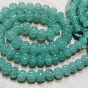 Può includere: Una collana di perline rotonde sfaccettate di colore azzurro chiaro. Le perline sono infilate su un filo trasparente e sono disposte in un motivo circolare.