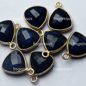 Puede incluir: Siete colgantes triangulares de piedra preciosa azul oscuro con engastes de metal dorado y anillas de salto.