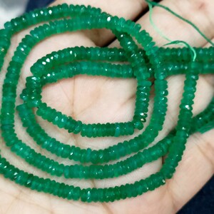 Op de afbeelding: Een streng groene edelsteen kralen. De kralen zijn gefacetteerd en hebben een licht onregelmatige vorm. De kralen zijn geregen op een dun draad en zijn klaar om te worden gebruikt voor het maken van sieraden.