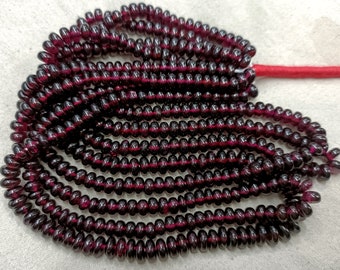 May include: Strands of dark red, disc-shaped beads. The beads are strung together on a red cord, creating a layered effect. The beads have a glossy finish and appear to be made of a translucent material.