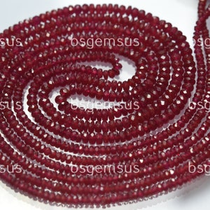 May include: A strand of deep red ruby beads, faceted and round, with a smooth, polished finish. The beads are strung together to form a long necklace or bracelet.