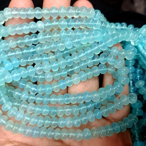 May include: A strand of light blue gemstone beads. The beads are round and smooth, and they have a translucent appearance.