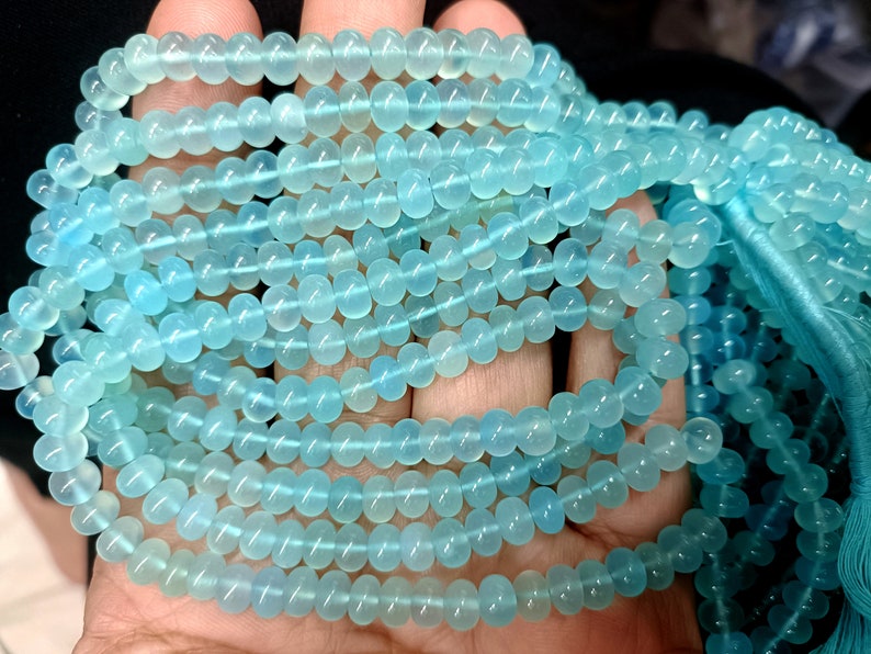 May include: A strand of light blue gemstone beads. The beads are round and smooth, and they have a translucent appearance.