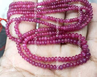 May include: A strand of pink ruby beads, approximately 3mm in diameter, with a smooth, polished finish. The beads are strung on a clear thread and are arranged in a loose, flowing pattern.
