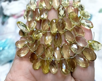 Puede incluir: Hilos de gemas de citrino facetadas en forma de lágrima, en varios tonos de amarillo y ámbar. Las gemas están ensartadas, mostrando sus superficies pulidas y su claridad interna. Ideales para la creación de joyas, estas cuentas ofrecen una paleta cálida.