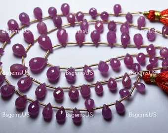 May include: Multiple strands of pink-red, faceted, teardrop-shaped gemstones strung on gold-coloured wire. The beads vary in size and are arranged in rows. Red tassels are visible at the ends. The image is watermarked with the text "bsgemsUS".
