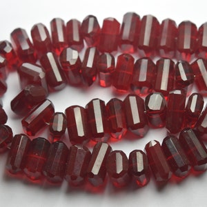 May include: A strand of dark red faceted glass beads. The beads are long and rectangular in shape.
