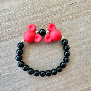 May include: A red and black beaded bracelet with two red Mickey Mouse head charms. The bracelet is made with black onyx beads and gold accents.