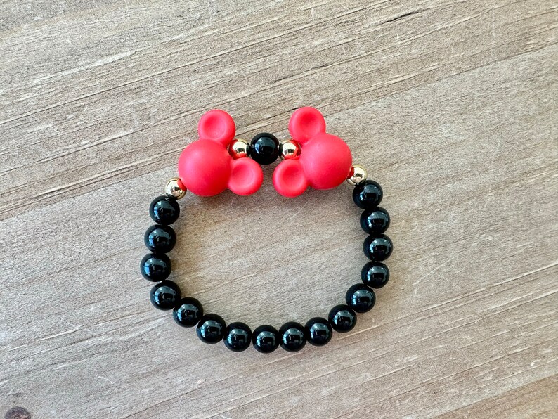 May include: A red and black beaded bracelet with two red Mickey Mouse head charms. The bracelet is made with black onyx beads and gold accents.