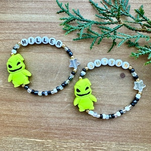 Puede incluir: Dos pulseras de cuentas con cuentas negras y blancas, estrellas doradas y dijes verdes de Jack Skellington. Las pulseras deletrean los nombres "MILLER" y "SUTTON".