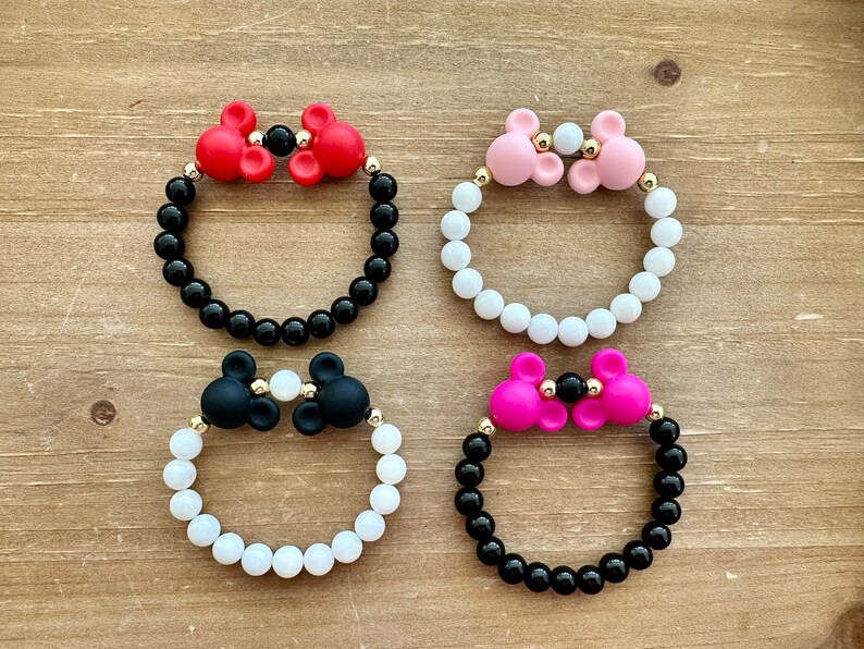 May include: Four bracelets with black and white beads and silicone Mickey Mouse ears in red, pink, black, and white.