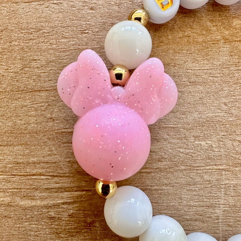 May include: A pink and white bracelet with a pink Minnie Mouse head charm. The charm has glitter on it.