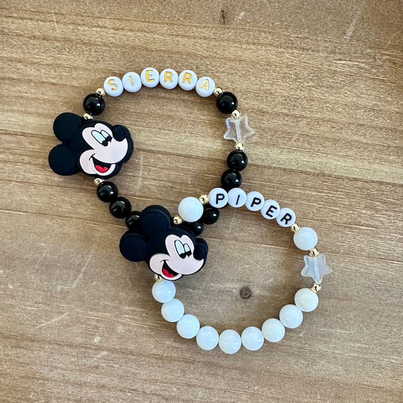 Puede incluir: Dos pulseras de cuentas blancas y negras con dijes de Mickey Mouse y cuentas de letras doradas que deletrean los nombres "SIERRA" y "PIPER".