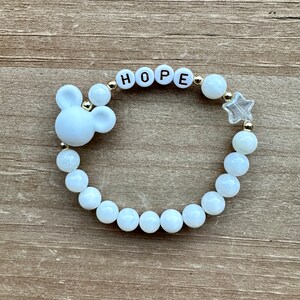 May include: White beaded bracelet with a Mickey Mouse charm, gold beads, and the word "HOPE" spelled out in white beads.