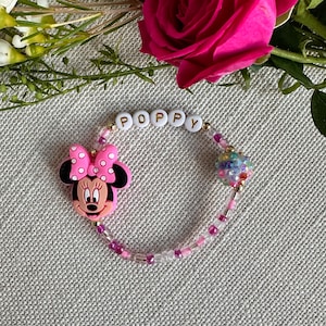 May include: A pink and white Minnie Mouse charm bracelet with a sparkly bead and white letter beads spelling "POPPY".