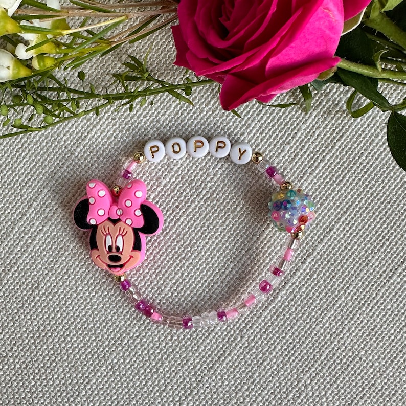 May include: A pink and white Minnie Mouse charm bracelet with a sparkly bead and white letter beads spelling "POPPY".