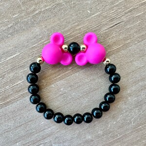 May include: A black beaded bracelet with two pink silicone mouse ears and gold accents.