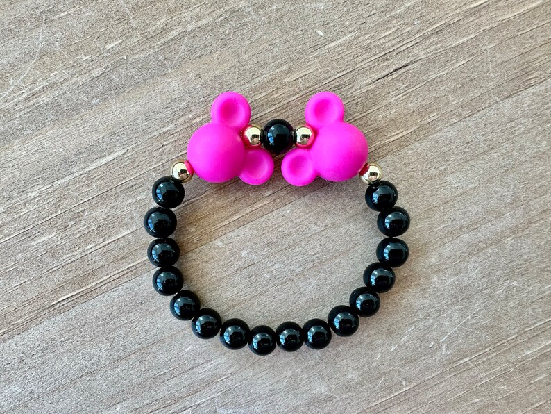 May include: A black beaded bracelet with two pink silicone mouse ears and gold accents.