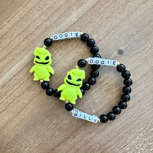 Puede incluir: Dos pulseras de cuentas negras con abalorios de personajes verdes de Oogie Boogie. Una pulsera tiene el nombre "Oogie" escrito en letras blancas sobre cuentas negras. La otra pulsera tiene el nombre "Billy" escrito en letras blancas sobre cuentas negras.