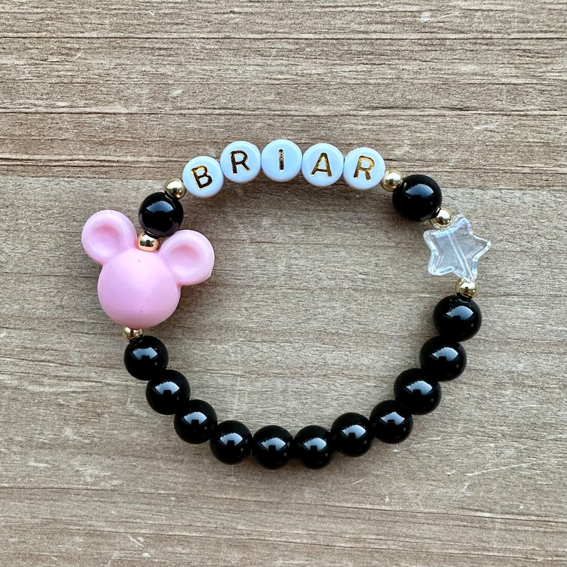 May include: A black beaded bracelet with a pink Mickey Mouse charm, a clear star charm, and white beads spelling "BRIAR".