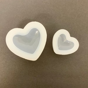 May include: Two white silicone heart-shaped moulds. The larger mould is about 10 cm wide and the smaller mould is about 5 cm wide.